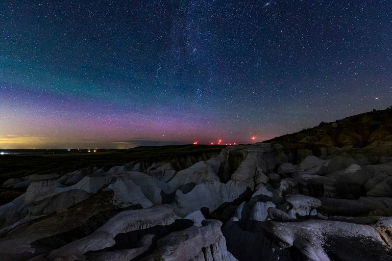 Paint Mines Colorado aurora with lights on the horizon with alien rocks in the foreground and lots of stars